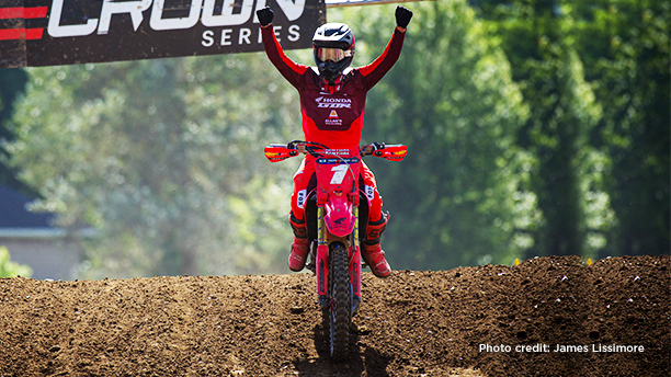 A Honda racer on his bike on a track, raising his arms in victory. Photo credit to James Lissimore.