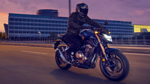 Un cavalier sur une moto Honda Standard au crépuscule avec des nuages ​​roses en arrière-plan