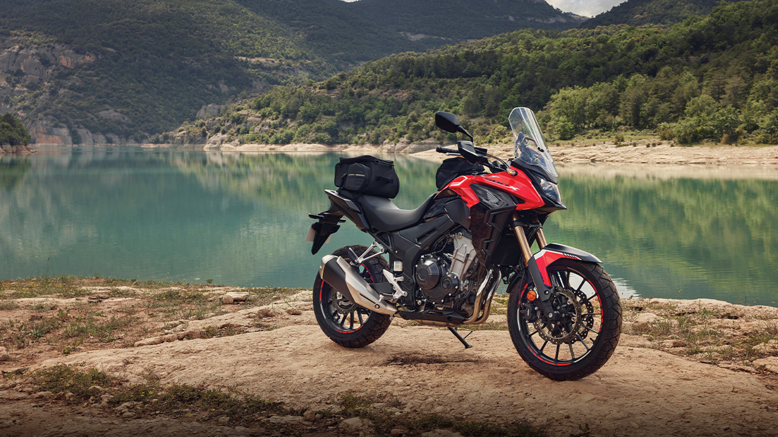 Un CB500X rouge stationné à côté d'un lac bleu