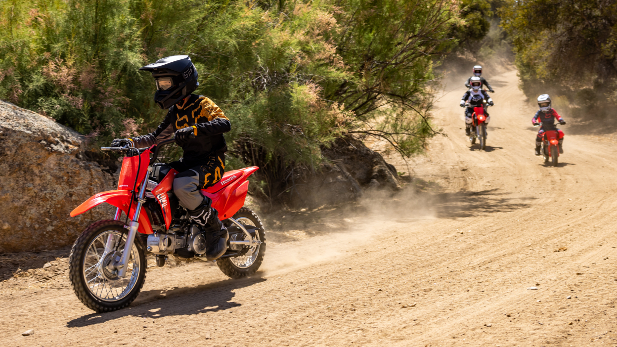 One young riders on dirt track ahead of three riders in background.