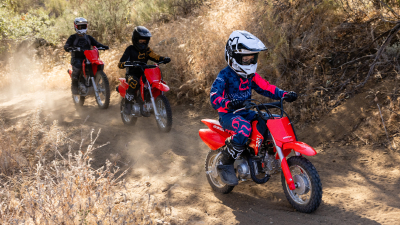 Three young riders on dirt track. Rider in front has a White helmet on.