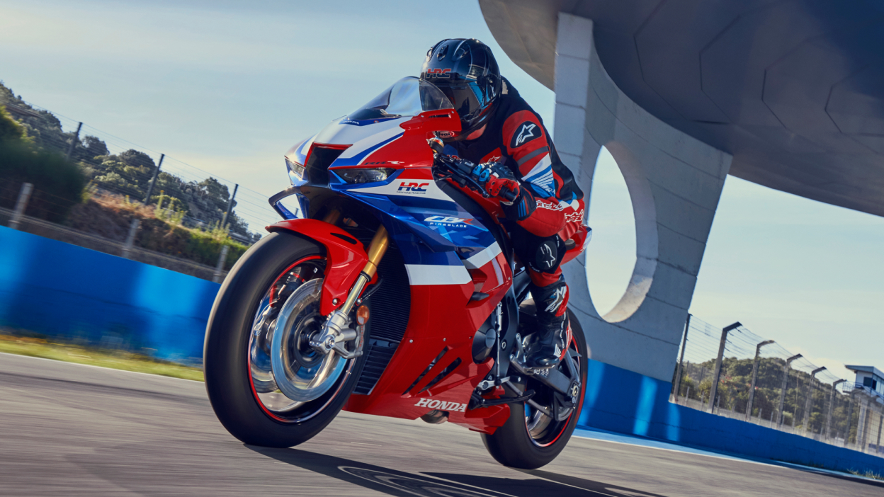 Left angle of Driver on Grand Prix Red Fireblade on track at high speed. Concrete structure above driver in background.