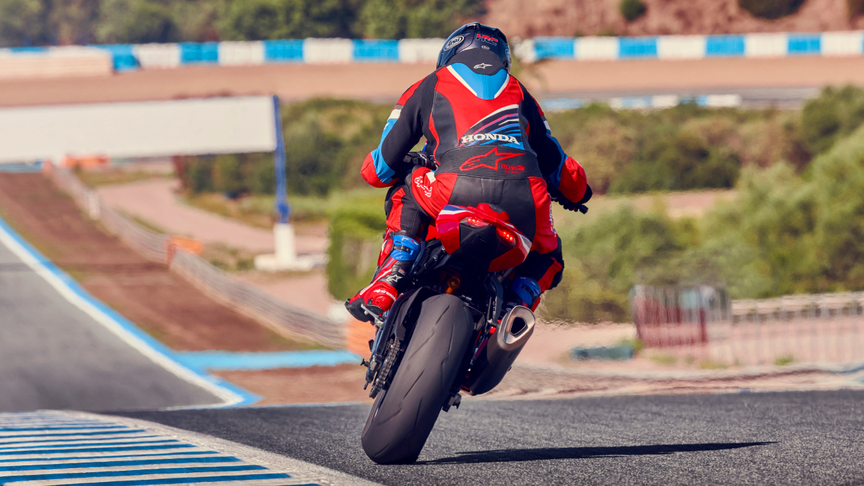Rear view of Driver on Grand Prix Red Fireblade on track. Leaning right. Bushes in background.