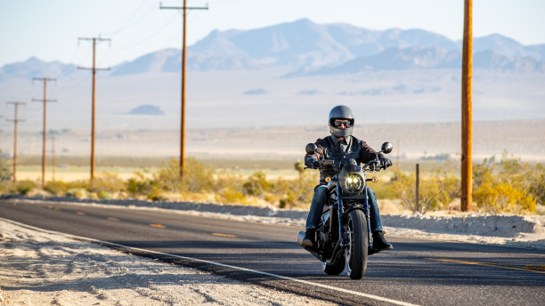 Un motard sur une moto roulant sur une autoroute du désert.  /  A biker on a motorcycle driving down a desert highway.