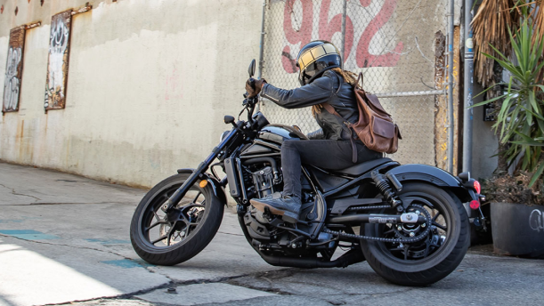 a rider on a Honda motorcyle wearing a backpack in an urban setting/ un pilote sur une moto Honda portant un sac à dos en milieu urbain